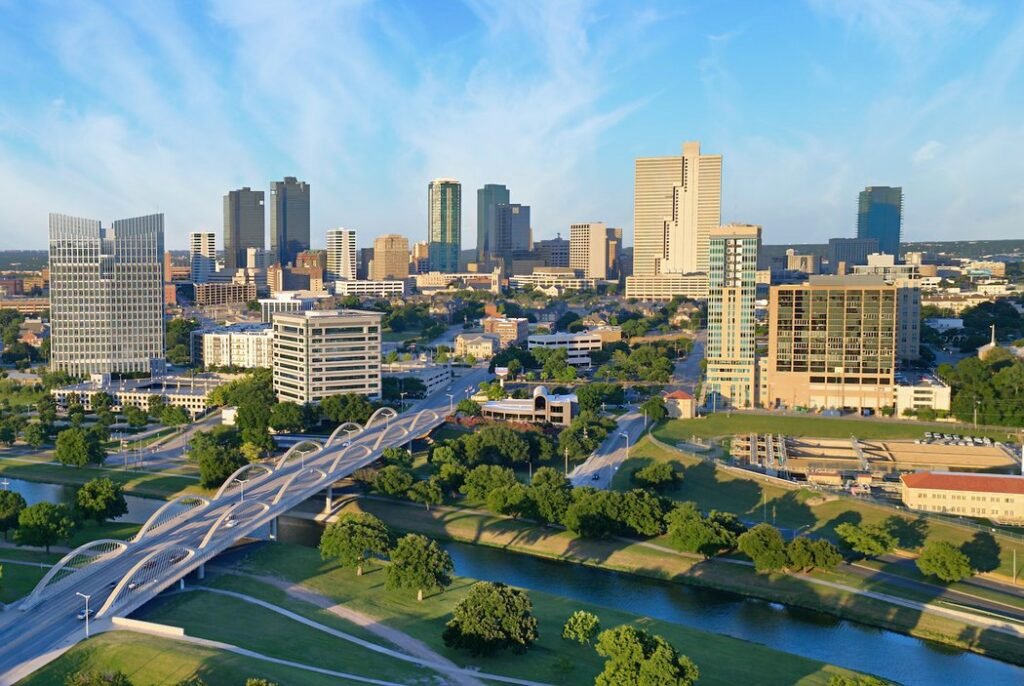 Aerial view of downtown cityscape with modern skyscrapers, river, green spaces, and bridge infrastructure.