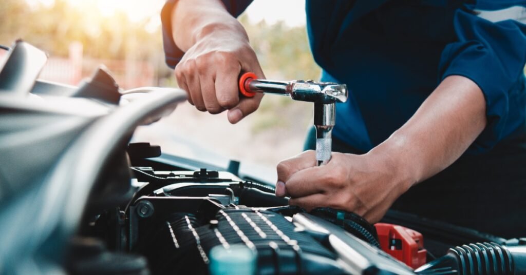 A close-up of a person inspecting a car engine with a torque wrench while standing outdoors beside a parked vehicle.