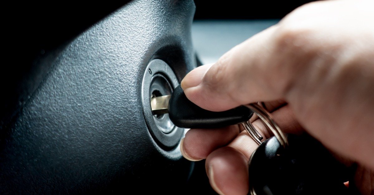 A close-up of a person turning a car key in the ignition switch to start the engine.