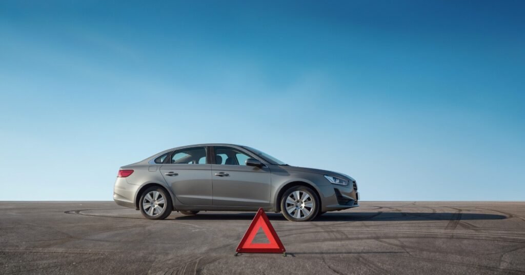 A gray car parked on open pavement behind a red warning triangle under a clear blue sky with tire marks nearby.